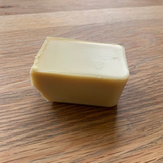 A rectangular bar of pale yellow wood polish standing upright on a brown wooden surface.
