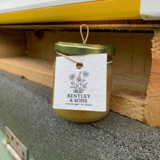 A Jar of Bentley and Sons Soft Set Honey in front of a beehive