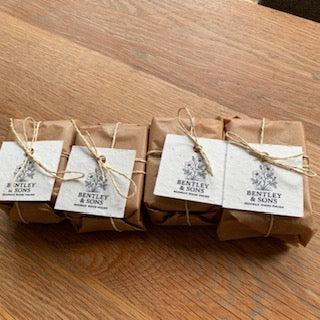 Three small wrapped gift boxes tied with twine and labeled Bentley & Sons, placed on a wooden tabletop.