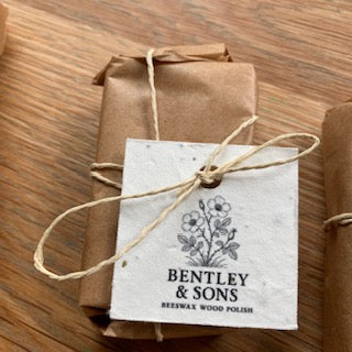 A small wrapped package tied with twine and a paper tag reading 'BENTLEY & SONS' and 'BEESWAX WOOD POLISH,' placed on a wooden surface.